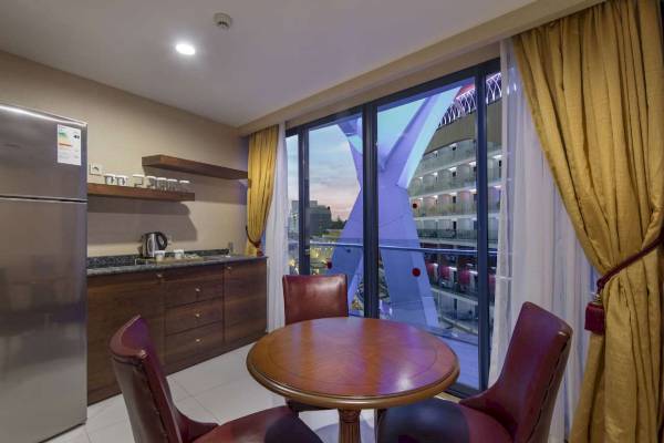 Innenansicht eines Zimmers im Granada Luxury Okurcalar Hotel mit Tisch, Stühlen und Kühlschrank.