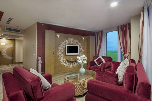 Wohnzimmer im Granada Luxury Okurcalar Hotel mit roten Sofas, Fernseher und Glastisch.