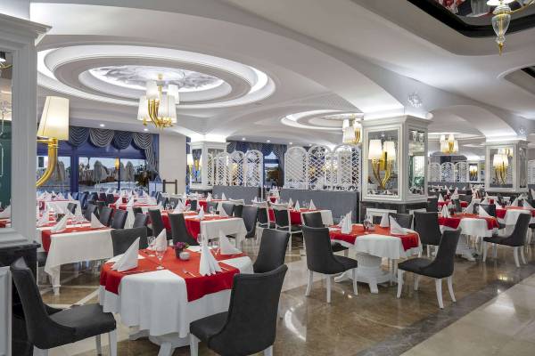 Restaurant im Granada Luxury Okurcalar Hotel mit weißen und roten Tischdecken und goldenen Kronleuchtern.