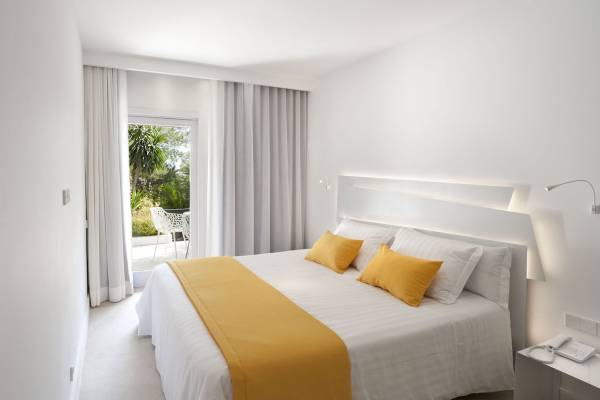 Hotelzimmer im Paraiso de los Pinos mit Bett, gelber Bettdecke, weißem Kopfteil und Zugang zur Terrasse.
