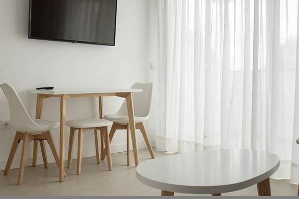 Innenbereich eines Zimmers im Hotel Apartamentos Es Pujols mit Tisch, Stühlen, Fernseher und Vorhängen.