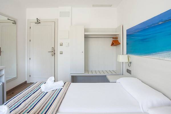 Rosales Formentera Hotelzimmer mit weißem Bett, Decken, Kissen und Badezimmerspiegel.