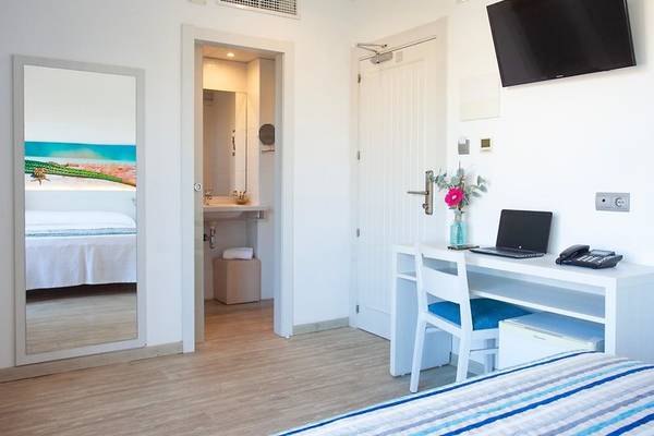 Innenansicht eines Hotelzimmers von Rosales Formentera, mit Schreibtisch, Laptop, Telefon und Fernseher.