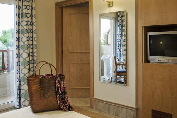 Ein Zimmer im Hotel Voramar Formentera mit einer offenen Tür, einem Spiegel, einem Fernseher und einem Korb auf dem Bett.