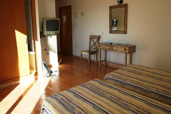 Ein Hotelzimmer mit zwei Betten, einem Fernseher an der Wand, einem Tisch mit Stuhl und einem Spiegel.