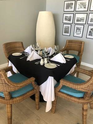 Speisetisch im Sands Barbados Hotel, gedeckt für vier Personen, mit Blick auf eine Wand mit schwarzen und weißen Fotorahmen.