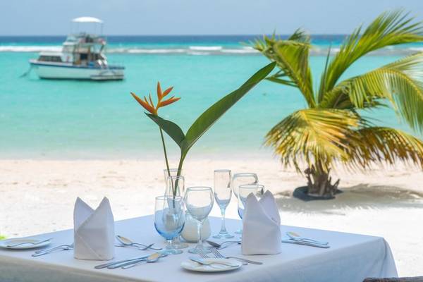 Ein Tisch auf dem Strand des Sands Barbados Hotels mit Blick auf das Meer und eine Palme.