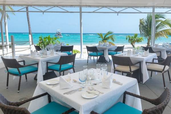 Außenbereich des Sands Barbados Hotels mit gedeckten Tischen und Stühlen am Strand.