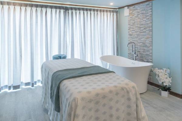 Massageraum im Sands Barbados mit Behandlungsliege, Badewanne und weißen Vorhängen.