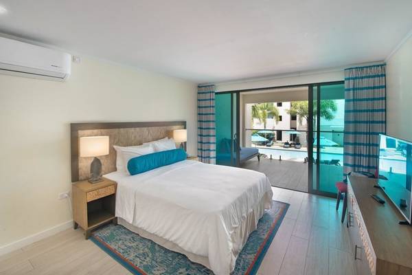 Innenansicht eines Hotelzimmers im Sands Barbados mit Bett, Klimaanlage, Fernseher und Glastür zu einem Poolbereich.