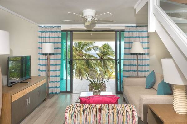 Wohnzimmer mit Meerblick im The Sands Barbados, mit Sofa, Fernseher und großer Glastür.