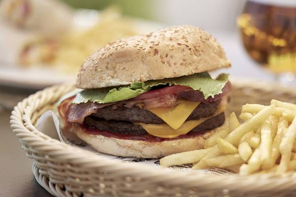 Ein Burger mit Pommes in einem Korb auf einem Tisch neben einem Glas Bier.