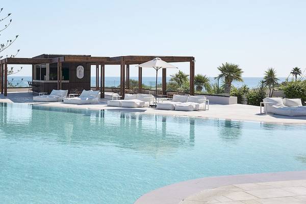 Poolbereich des Helea Lifestyle Beach Resorts mit Blick auf das Meer und weißen Liegestühlen