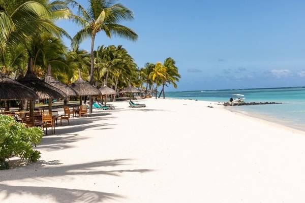 Strand mit weißen Palmen, Sonnenliegen und einem Boot am Paradis Beachcomber Golf Resort & Spa.