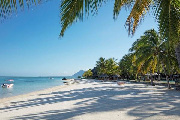 Strand des Paradis Beachcomber Golf Resort & Spa mit weißen Palmen und Booten im Hintergrund