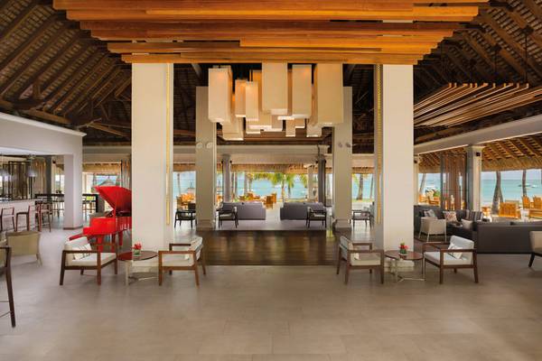 Lobby des Paradis Beachcomber Golf Resort & Spa mit Klavier, Tischen, Sesseln und Blick auf den Strand