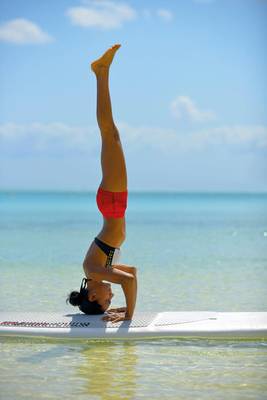 Eine Frau praktiziert Yoga auf einem Surfbrett im Wasser.