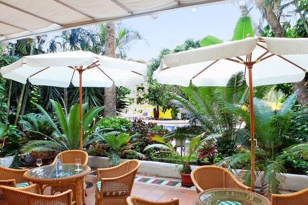 Terrasse des H10 Tenerife Playa Hotels mit Tischen, Stühlen und Sonnenschirmen.