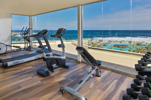 Fitnessraum im H10 Tenerife Playa Hotel mit Blick auf das Meer und einen Swimmingpool.