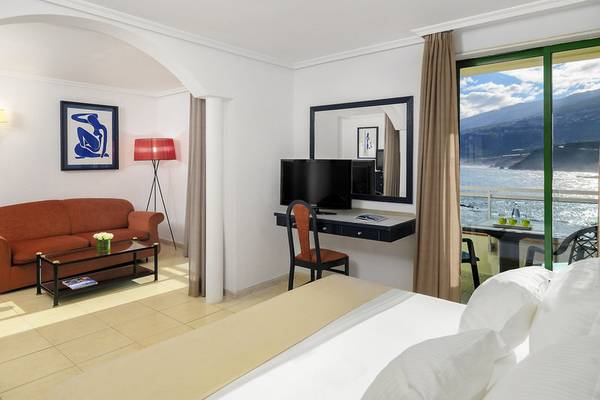 Ein Hotelzimmer im H10 Tenerife Playa mit Blick auf das Meer, einem großen Bett, einem Schreibtisch und einer Couch.