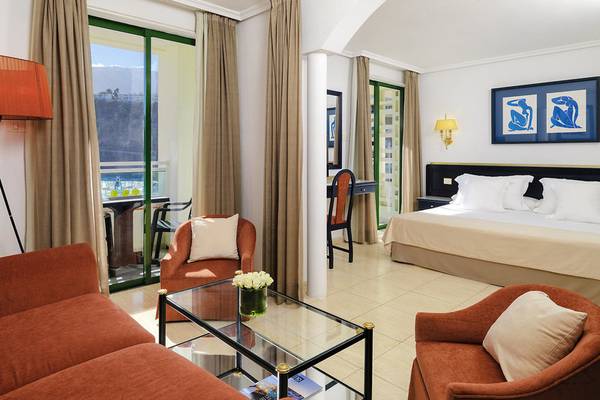 Schlafzimmer des H10 Tenerife Playa Hotels mit Doppelbett, Sesseln und Tisch.