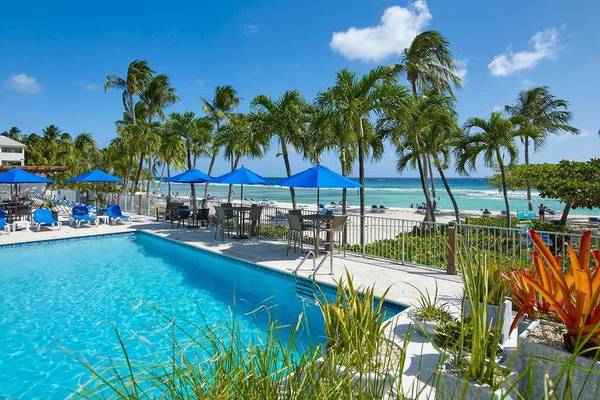 Poolbereich des Coconut Court Beach Hotels mit blauen Sonnenschirmen und Blick auf den Strand.