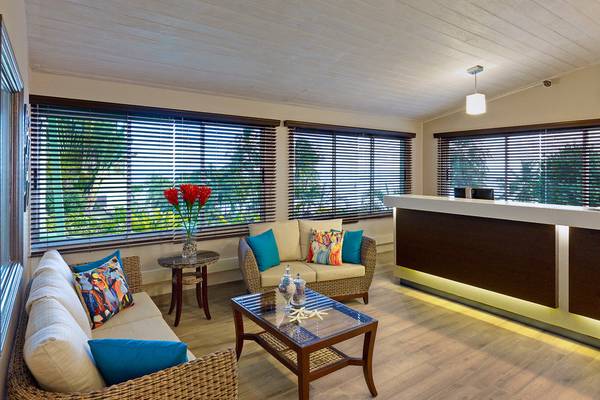 Innenansicht der Lobby des Coconut Court Beach Hotels mit hellem Holzboden, großen Fenstern und stilvollen Möbeln.
