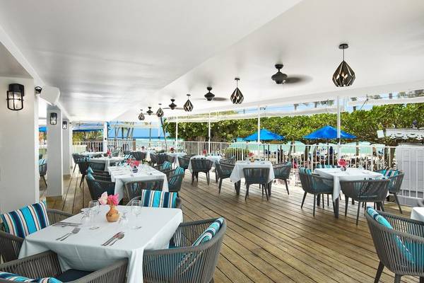 Terrasse des Coconut Court Beach Restaurants mit Tischen und Stühlen und Blick auf den Ozean.