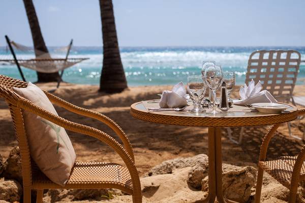 Strandtisch mit Getränken und Stühlen im Hintergrund Palmen und Meer