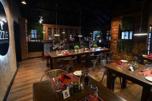 Innenansicht eines Restaurants mit rustikalem Design, Holztischen, Stühlen und dekorativen Elementen.