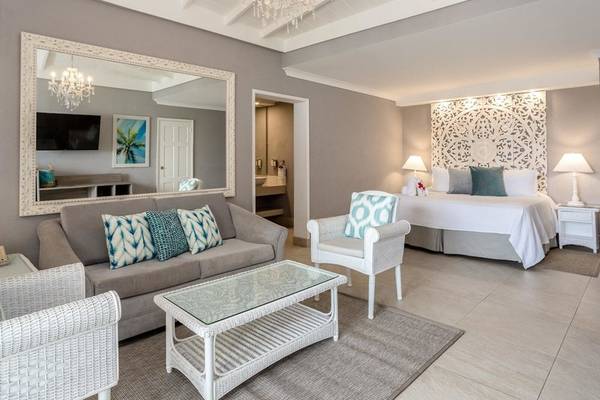 Innenansicht der Suite im Sugar Bay Barbados Hotel mit grauem Sofa, weißem Tisch und großem Spiegel.
