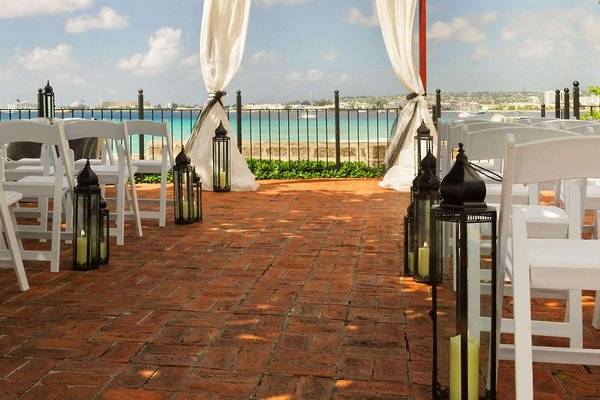Hochzeitszeremonie unter freiem Himmel im Hilton Barbados mit weißen Stühlen und roten Laternen.