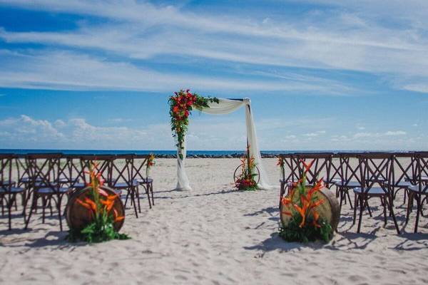 Hochzeitszeremonie auf dem Strand des Hilton Barbados mit Blumenbogen und Stühlen.