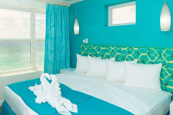 Schlafzimmer im Rostrevor Hotel mit türkisfarbenen Wänden, Blick auf das Meer und ein Bett mit weißen Kissen und türkisen Laken.