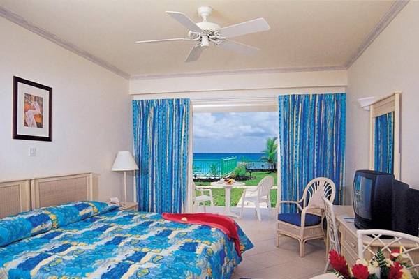 Ein Zimmer im Rostrevor Hotel mit Blick auf das Meer, blauen Vorhängen, einem Bett, einem Fernseher und einem Tisch mit einem Strauß Blumen.