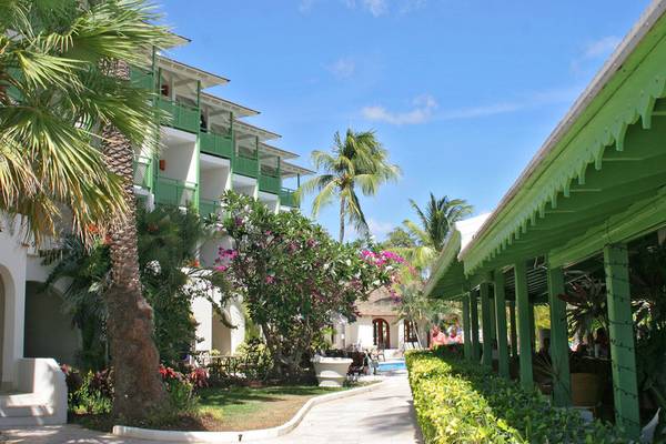 Außenansicht des Mango Bay Hotel mit grünen Gebäuden, Palmen und einem Pool im Hintergrund.
