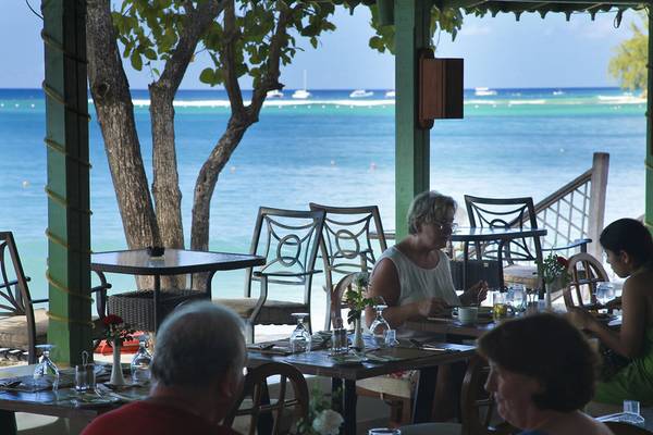 Gäste sitzen an Tischen auf der Terrasse des Mango Bay Hotels mit Blick auf das Meer.