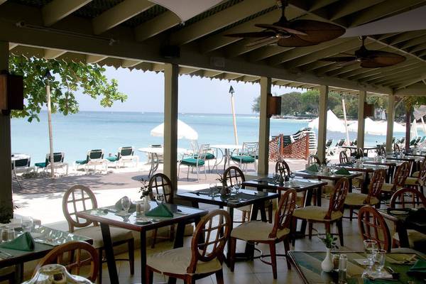 Restaurantterrasse des Mango Bay Hotels mit Blick auf das Meer und Sonnenliegen.