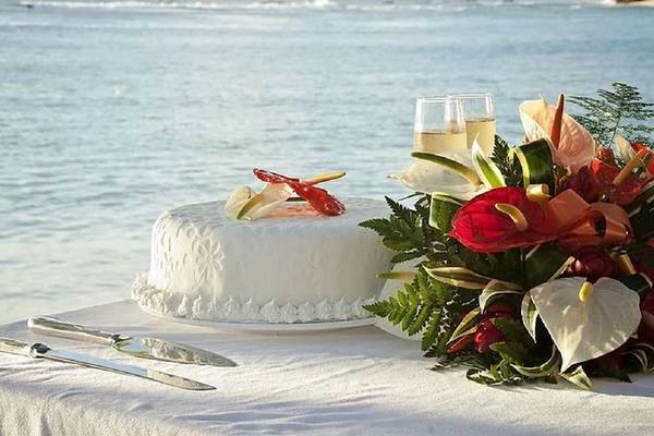 Hochzeitstorte am Strand des Mango Bay Hotels mit Meer im Hintergrund.