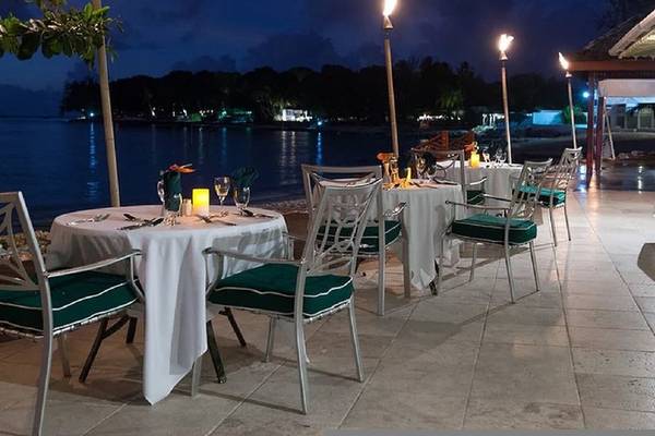 Außenbereich mit Tischen und Stühlen, beleuchtet, Blick auf das Meer bei Nacht, Mango Bay Hotel.
