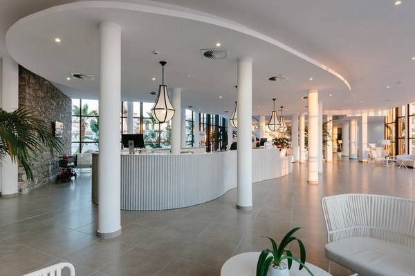 Empfangsbereich des AluaSoul Ibiza Hotels mit gebogener Theke, weißen Möbeln und Pflanzen.