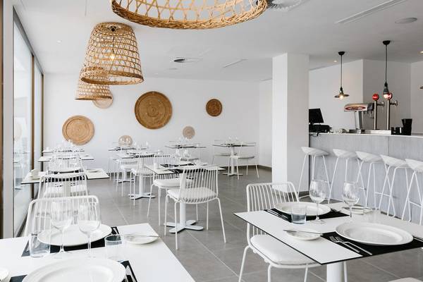 Innenansicht des AluaSoul Ibiza Restaurants mit weißen Tischen und Stühlen, großen Fenstern und Holzlampen.