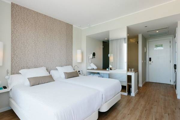 Innenansicht eines Doppelzimmers im AluaSoul Ibiza Hotel mit zwei Betten, Nachttischen und einer Eingangstür.