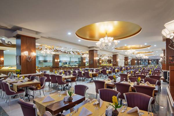 Innenansicht des Restaurants im Alan Xafira Deluxe Resort & Spa mit gedeckten Tischen, Kronleuchtern und blauen Stühlen.