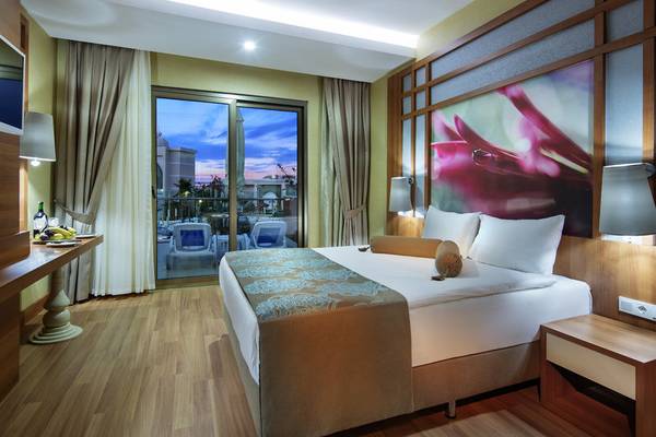 Hotelzimmer mit großem Bett, Fenstern und Balkon mit Blick auf die Stadt.