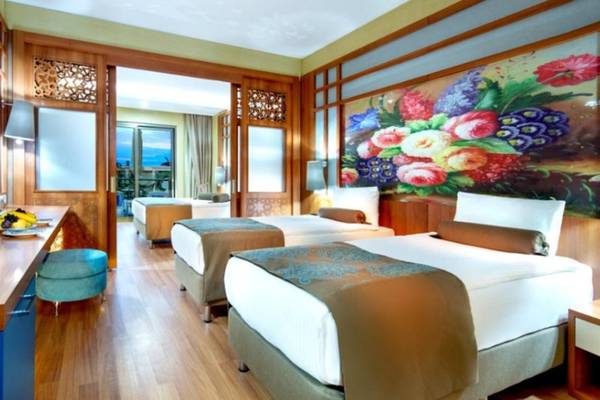 Hotelzimmer mit drei Betten, einem Schreibtisch und einem großen Blumenwandgemälde.