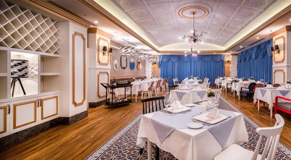 Innenansicht des Restaurants im Sensitive Premium Resort & Spa, mit gedeckten Tischen, blauen Vorhängen und Holzboden.