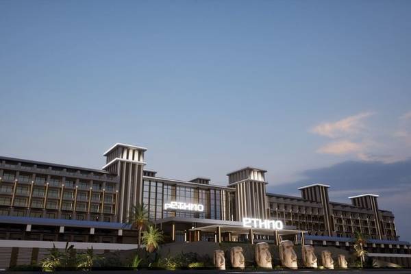 Außenansicht des Ethno Belek Hotels mit Statuen und moderner Architektur bei Sonnenuntergang.