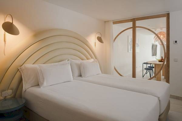 Schlafzimmer im Plus Fariones Suite Hotel mit zwei weißen Betten, Kissen und Lampen.