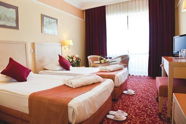 Drei Betten im Richmond Ephesus Resort Hotelzimmer mit roten Vorhängen und Tisch.